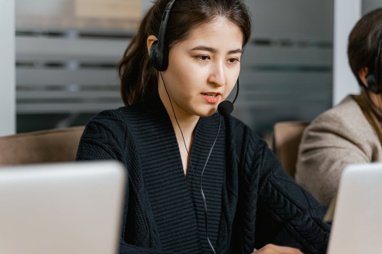 about-img Asian woman in a call center focused on customer support tasks using a laptop.